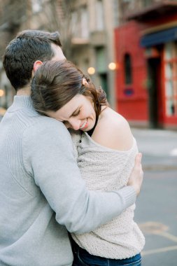 Güzel beyaz bir çift, şehir ortamında samimi bir kucaklaşmada hareketsiz duruyor.