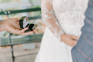 Bir insan zarif bir kutuda eşine yüzük sunar. İkisi de güzel bir bahçede özel bir durum için giyinir..