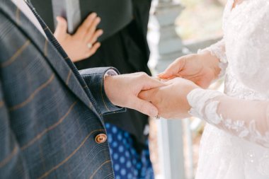 İki birey, düğün törenlerinin hassas bir anında güzel bir açık hava mekanının altında el ele tutuşuyorlar..