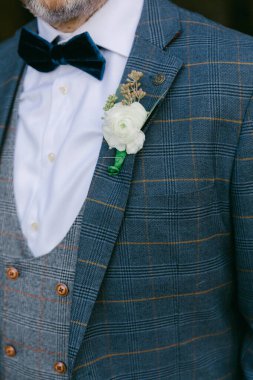 Şık damat, düğün sırasında taze çiçek yaka çiçeğiyle süslenmiş ekose bir takım elbise ve papyon sergiliyor..