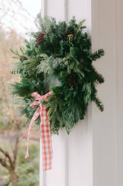 Çam kozalaklarıyla süslenmiş taze bir yeşil çelenk ve sonbaharda verandada kırmızı kareli bir kurdele sergilenir..