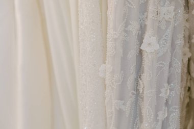 Bir butikte asılı narin gelinliklerin çeşitliliği ayrıntılı süslemeleri ve dokuları vurguluyor..