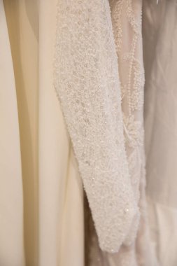 Detaylı boncuk işi bir gelin butiğinde asılı zarif bir gelinliği süslüyor, gelinlik ilhamı ve tarzı sergiliyor..