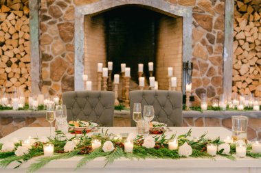 Kış kutlamaları için sıcak taş şöminenin yanında taze çiçekler ve mumlarla süslenmiş güzel bir yemek masası..