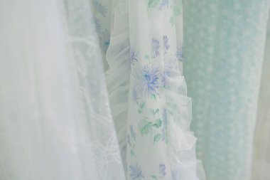 Çiçekli yumuşak pastel kumaş parlak bir odada asılı, yumuşak gölgeler bırakıyor ve sükunet katıyor..