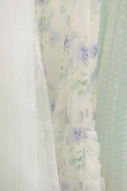 Çiçek desenli ve açık renkli kumaşlar bir giyim mağazasında zarifçe asılı duruyor ve sakin bir alışveriş ortamı yaratıyor..