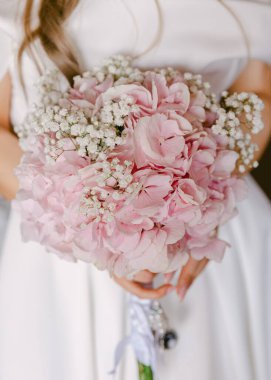 Bir gelin, özel günü için göz kamaştırıcı bir buket açık pembe ortanca ve bebek nefesi tutar..