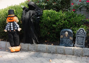 Sonbaharda bir bahçede, karanlık bir figür ve iki mezar taşının yanında duran şapkalı bir korkuluk..