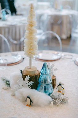 Şenlikli masa süsü, sıcak kış atmosferinde beyaz ağaçlar, mavi süslemeler, penguenler ve kar taneleri sergiliyor..