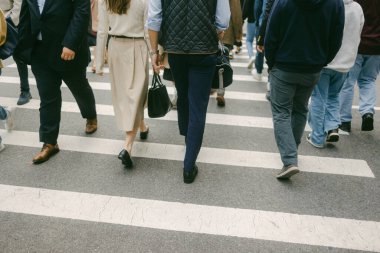 Güneşli bir günde yaya geçidinde şehir binalarıyla çevrili bir yaya geçidi kalabalığı.