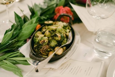 Taze pişmiş Brüksel lahanaları siyah bir tabakta sunuluyor süslü bir masa düzeninde, canlı yeşiller sergileniyor..