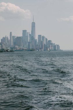 New York 'un ufuk çizgisi, yüksek binaları ve suyun üzerinde bulutlu bir gökyüzünü gösteriyor, sakin bir şehir manzarasını yakalıyor..