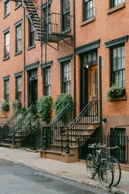 Brownstone evlerinde yeşil renkli merdivenler ve sakin bir cadde boyunca park edilmiş bisikletler yer alıyor..