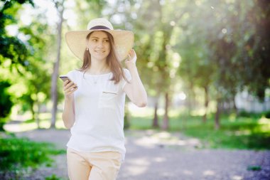 Elinde telefon olan mutlu kız, başında şapka var.