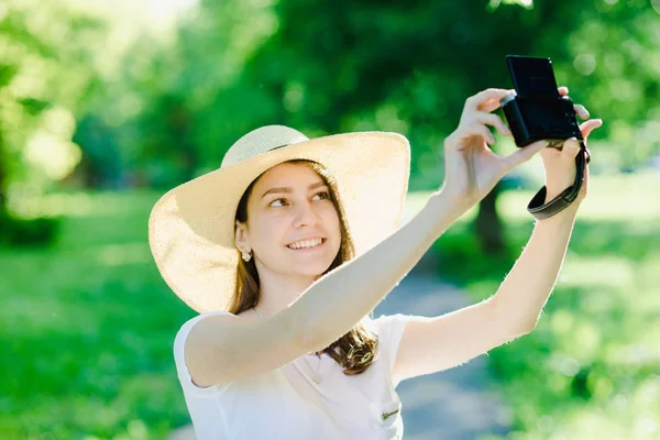 Elinde kamera olan bir kız, kafasında şapka var.