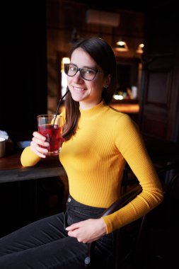 gözlük ve sarı bir balıkçı yaka kameraya bakarak bir pencere önünde kız kapalı