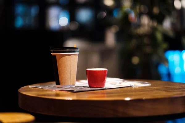 Bir fincan kahve ile alay et. Masada bir bardak, arka planda kahve satan bir kafede. Kahve lazım. Açık duvarlar. Ahşap masa. Cafe. Çiçek 