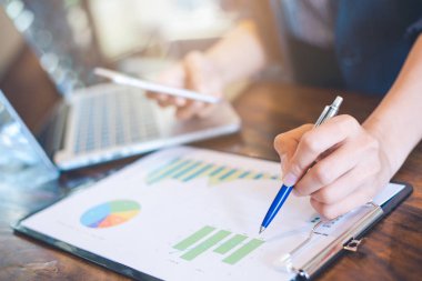 Sonuçları gösteren analiz çizelgeleri ve grafikler üzerinde çalışan bir işadamı. Elindeki kalem grafiğe işaret ediyor. İş analizi ve stratejisi..