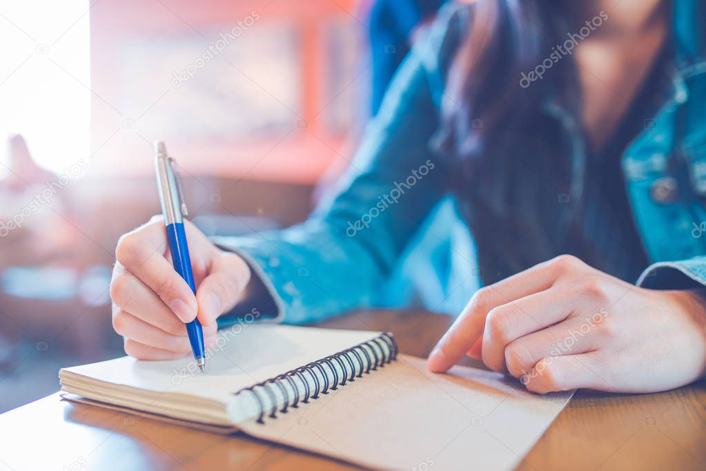 A woman's hand is writing in empty spiral notepad with a pen.