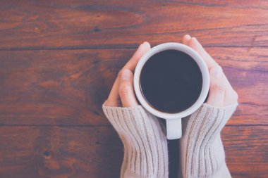 Sıcak kazaklı bir fincan kahve bir ahşap masa arka plan, üstten görünüm üzerinde tutan el kadın