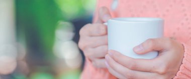 Bir fincan coffee.for Web afiş tutarak sıcak süveterin içinde el kadın.