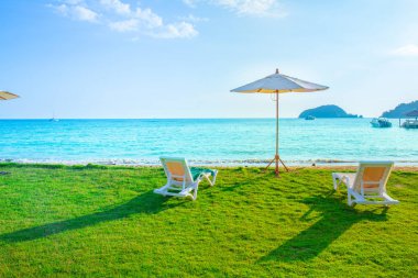 Beach chairs and beach umbrellas are on the lawn at the beach.Sea view and bright sky. clipart