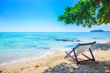 Plaj sandalyeleri ağaçların altında yer alan deniz ve dağ manzaralı.