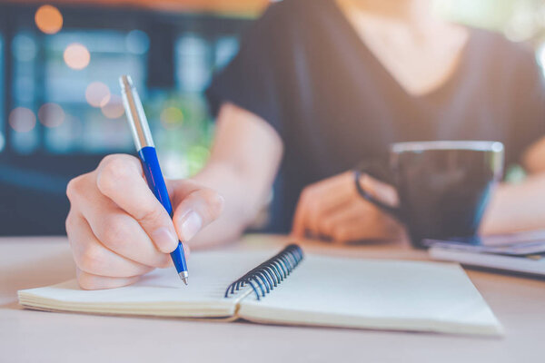 Business woman hand is writing on a notebook with a pen.