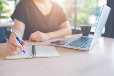 Kadın eli kalemle not etmek üstünde yazıyor. Masanın üzerinde orada