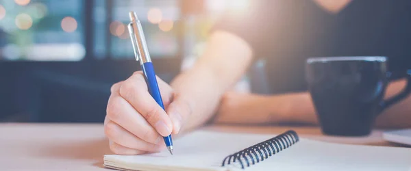 Mujer mano está escribiendo en un cuaderno con un bolígrafo en la oficina . — Foto de Stock