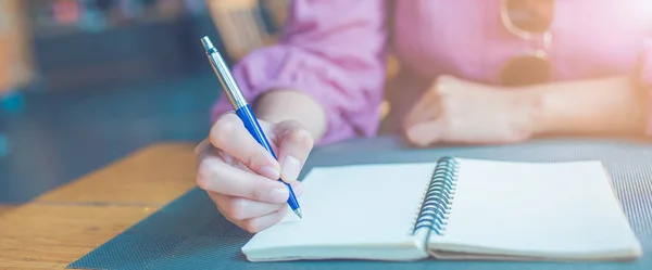 La mano de la mujer está escribiendo en un bloc de notas con un bolígrafo. . — Foto de Stock