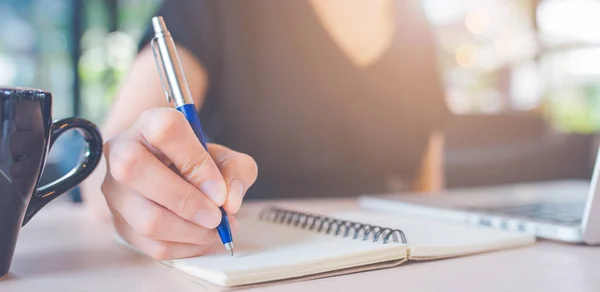 Mujer mano está escribiendo en un cuaderno con un bolígrafo . — Foto de Stock