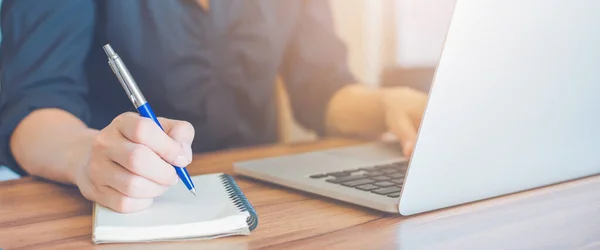 İş kadını kalemle bir deftere yazı yazıyor ve ofiste çalışmak için dizüstü bilgisayar kullanıyor. Web pankartı.