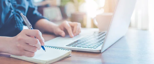İş kadını kalemle bir deftere yazı yazıyor ve ofiste çalışmak için dizüstü bilgisayar kullanıyor. Web pankartı.