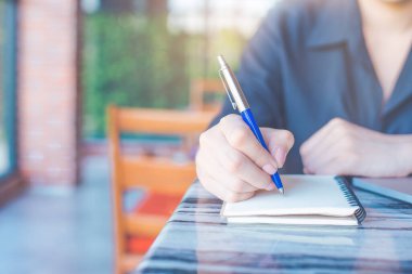 Kadın, ofisinde kalemle deftere yazı yazıyor..