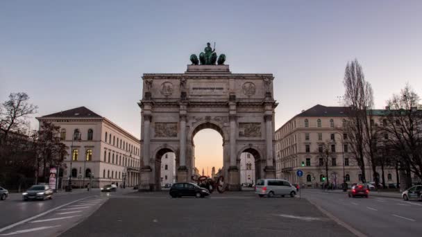 Alemania, Múnich - El Arco de la Victoria de Siegestor al atardecer con el tráfico que va alrededor del arco día a noche timelapse transición Video de stock