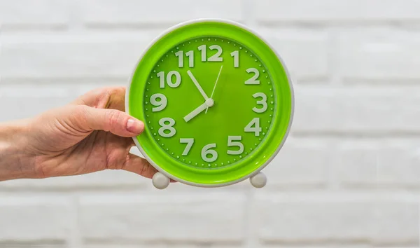 Green round clock in a female hand on a white background