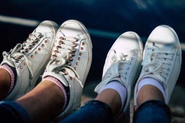 Dağların eteklerinde beyaz spor ayakkabılarla oturan insanlar.