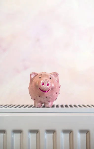 Piggy money box on heater at home. Energy consumption savings concept. Pink pig on radiator.