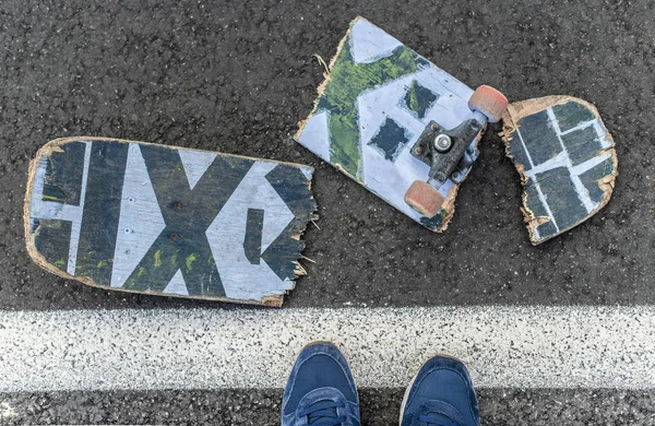 Kırık kaykay üzerinde karanlık asfalt sokak. Çocuk spor ayakkabı kaykay üzerinde adım attı. Sokak satırını.