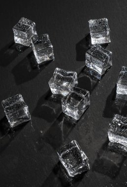 Siyah taş tahta üzerinde buz küpleri. Islak buz küpleri ile su damlaları. Sert ışık. Derin gölgeler. Soğuk ve tazelik kavramı. Yaz anlayışları içer. Koyu arka plan.