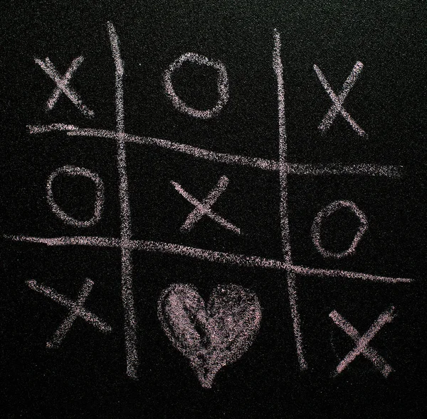 Tic-tac-toe game on black board. Valentines day concept with tic tac toy symbols written with chalk. XO XO symbols and heart shape.