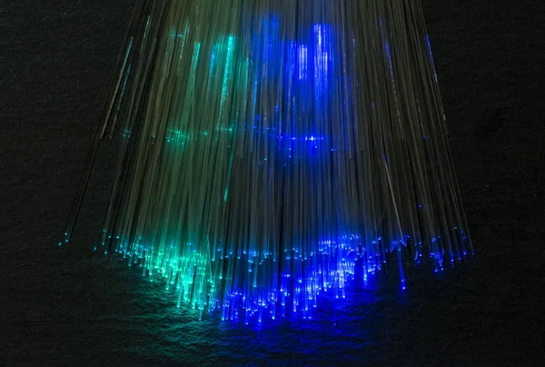 Colourful optic fibers illuminated on dark background. High speed internet concept. Data transfer optic fiber cable. Bunch of many optical fibers, glowing different colors. Technology background.