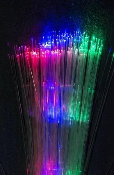 Colourful optic fibers illuminated on dark background. High speed internet concept. Data transfer optic fiber cable. Bunch of many optical fibers, glowing different colors. Technology background.