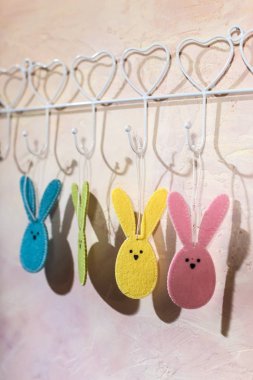 Paskalya tavşanı bir odada duvara kanca. Çok renkli Paskalya tavşanımı kumaş pembe duvar üzerine yapılmış. Sert ışık pencere ve duvar gölgeler. Beyaz vintage askı.