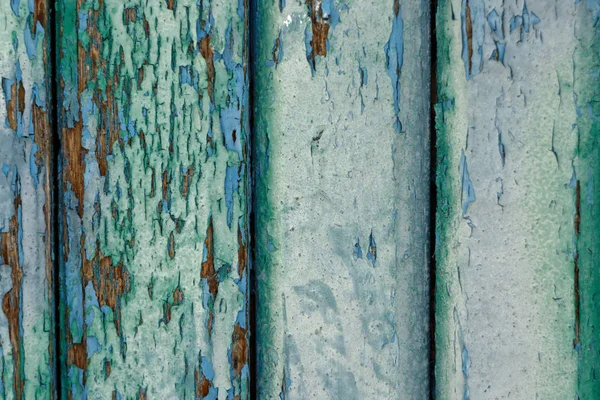 Old wooden boards painted with several layers of blue and green paints. The paint has peeled and faded from time to time.