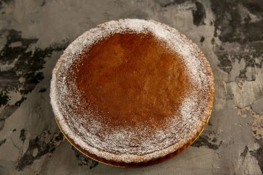 Pudra şekerli yuvarlak çikolatalı pasta koyu dokulu bir arka planda yatıyor.