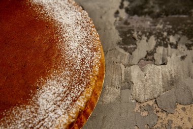 Pudra şekerli yuvarlak çikolatalı pasta koyu dokulu bir arka planda yatıyor.