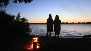 Gölgeler kamp ateşinin yanında iki kız güneşin doğuşunu selamlıyor. Kamp sabahı manzaralı açık hava konsepti