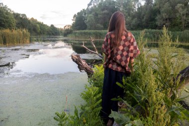 Doğadaki bir kızın silueti. Nehir ovası eski pürüzler, ördek yosunu ve sazlıklarla dolu. Dinyeper 'da dokunulmamış doğa ve günbatımı (Dnipro)